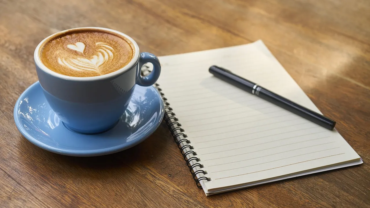 Tasse de café au lait décorée d’un cœur, à côté d’un carnet