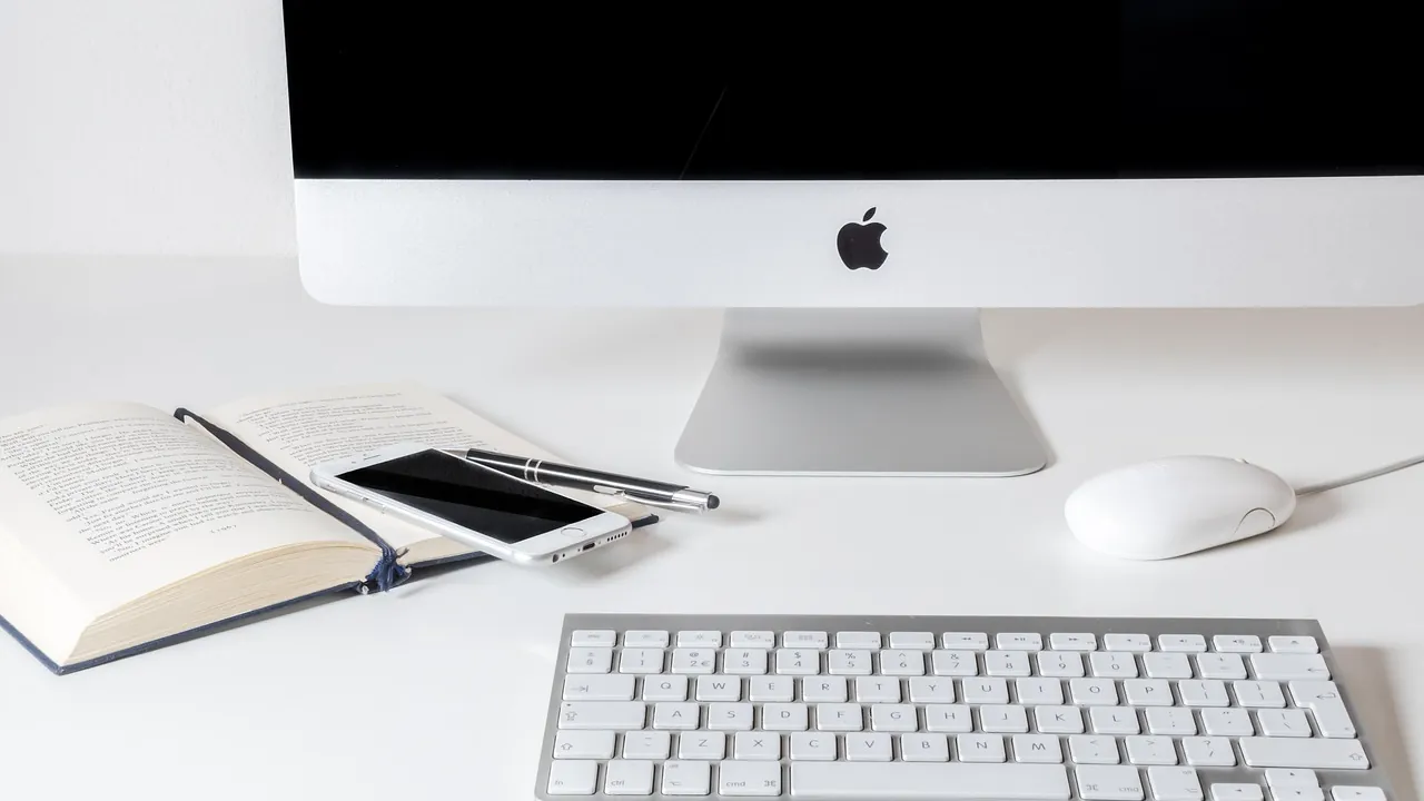 Bureau blanc avec écran, clavier et smartphone posé sur un livre ouvert